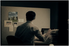한 남성이 컴퓨터 앞에 앉아 칠판에 붙여진 것을 바라보고 있는 사진